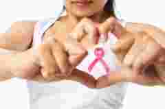 Heart framing from fingers on woman chest with pink badge to support breast cancer cause, PS: you can change the ribbon color to red to support AIDS cause as both using same symbol