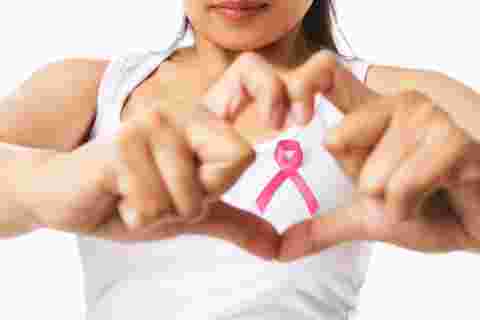 Heart framing from fingers on woman chest with pink badge to support breast cancer cause, PS: you can change the ribbon color to red to support AIDS cause as both using same symbol