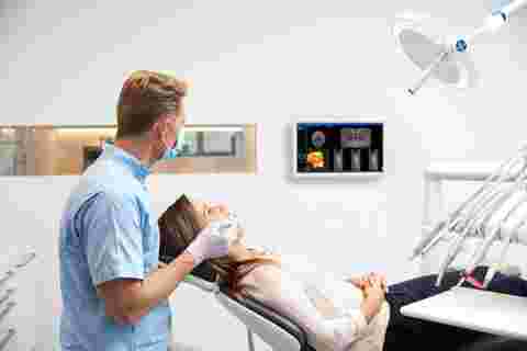 Dental practice with white Nio display wall-mounted, dentist, patient