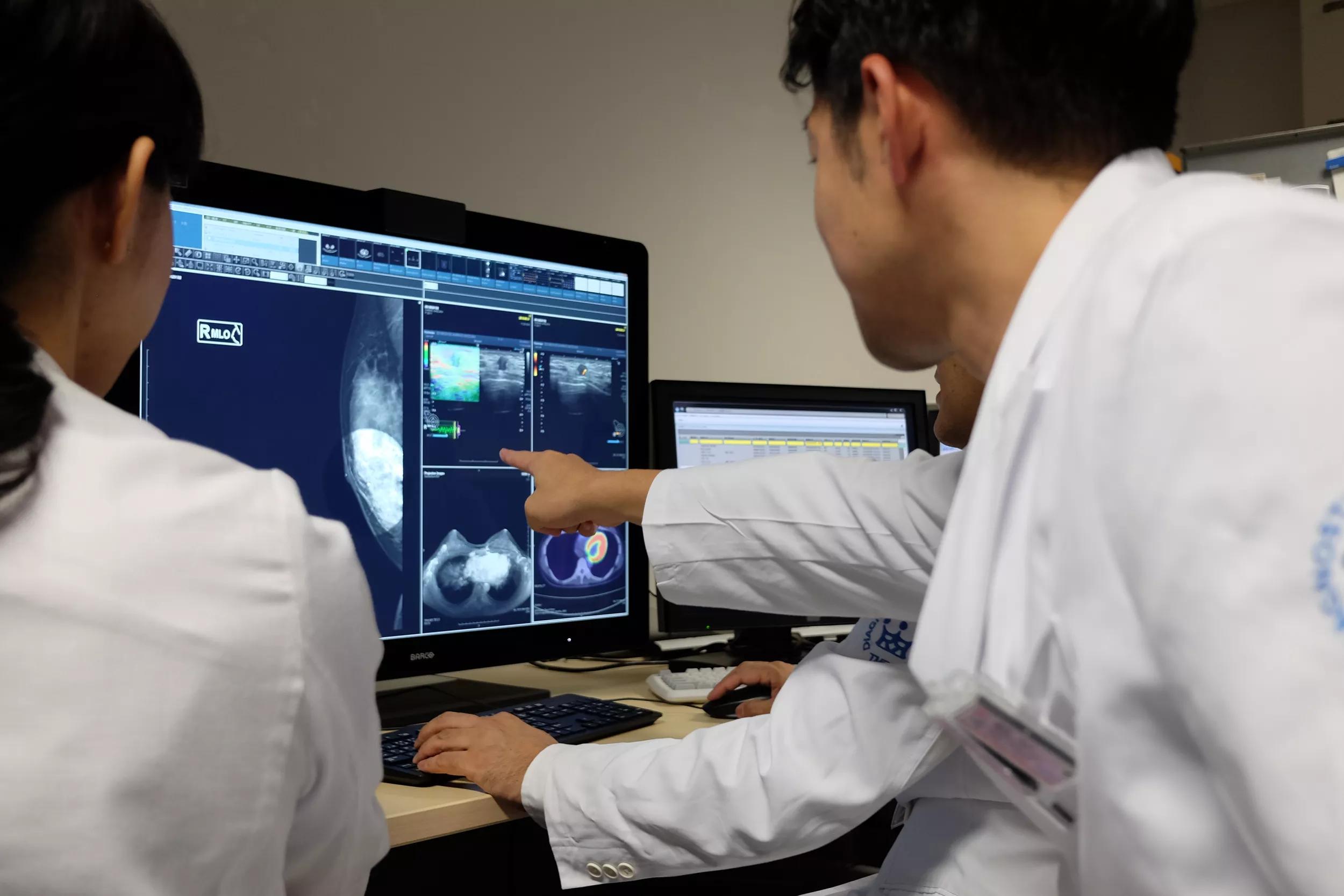 Radiologists looking at breast images together, one is pointing at something on the image
