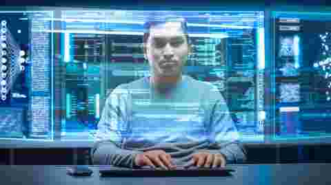 Portrait of Software Developer / Hacker Wearing Glasses Sitting at His Desk and Working on Futuristic Transparent Computer in Digital Identity Cyber Security Data Center. Hacking or Programming.