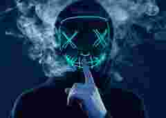 Close-up portrait of an anonymous man hiding his face behind a scary neon mask in a colored smoke. Studio shot