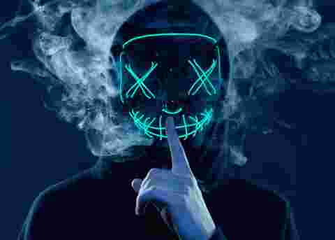Close-up portrait of an anonymous man hiding his face behind a scary neon mask in a colored smoke. Studio shot