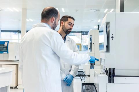 Two lab technicians in white coats and blue gloves are working with modern medical equipment, performing blood analysis in a scientific laboratory, indicating advanced diagnostics and healthcare
