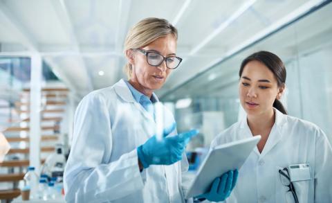 Women, scientist and discussion in lab with tablet, reading and review for experiment results at pharma company. People, mentor and feedback with solution, stats or medical research for mpox vaccine.