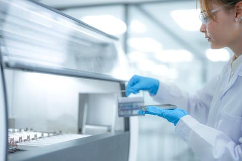 Focused female scientist loading a sample rack into an automated machine in a sterile clinical laboratory. Professional researcher working on pathology diagnosis for medical healthcare projects.
