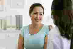 Female doctor reassuring smiling Vietnamese mature woman