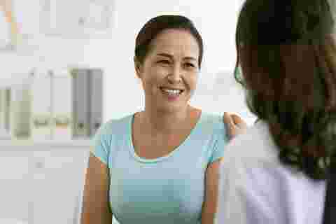 Female doctor reassuring smiling Vietnamese mature woman