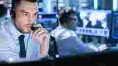 In Monitoring Room Technical Support Specialist Speaks into Headset. His Colleagues are Working in the Background. military & government