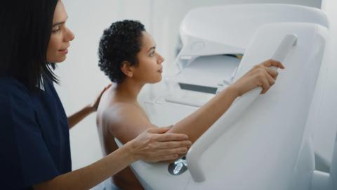 Friendly Female Doctor Explains the Mammogram Procedure to a Topless Latin Female Patient with Curly Hair Undergoing Mammography Scan. Healthy Female Does Cancer Prevention Routine in Hospital Room.