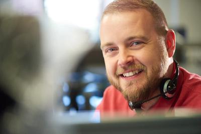 a young male customer services representative takes a moment off the phones to smile at camera